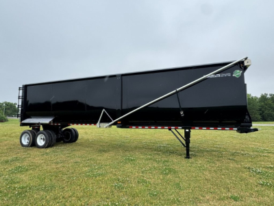 Armor Lite dump trailer with side panel and landing gear visible. Text on side reads Armor Lite; rear area shows support jack and wheels.