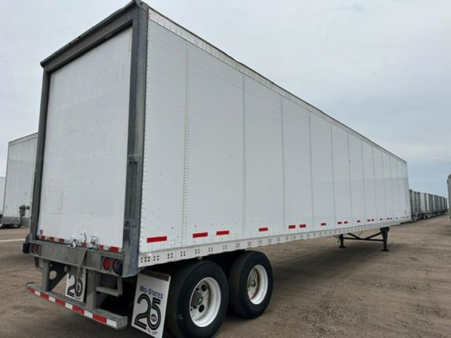 Trailer undercarriage in side view showing dual rear axles and white dry van body