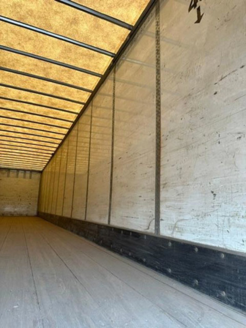 Trailer interior side walls with metal frame. Wood floor. Sunlight entering from translucent roof panels. No visible text or labels.