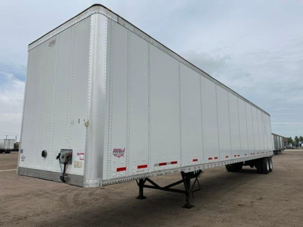 Trailer side of a white Wabash van trailer showing the front left corner and undercarriage; no visible text on the side, small rear access with hitch.