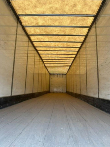Interior of a boxed trailer cargo area with yellow translucent roof, long narrow perspective, wooden floor and light walls.