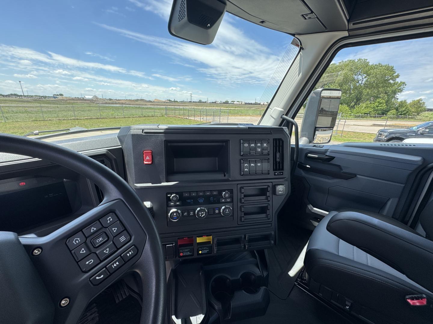 Interior of a Mack AN64T daycab truck cockpit showing steering wheel with control buttons, center console, dashboard gauges, and passenger seat.
