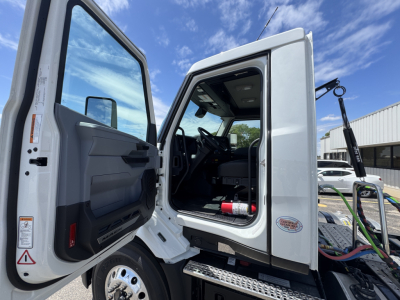 Truck cab interior and open door of a 2027 Mack AN64T daycab showing interior steering wheel, dashboard, and entry step.