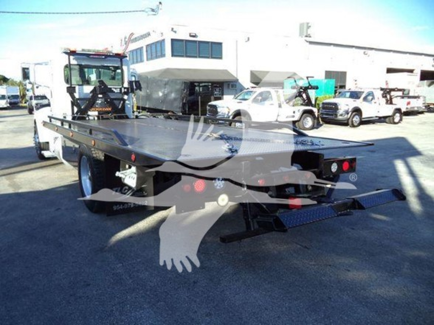 2020 Peterbilt 337 rollback truck in lot with flatbed, rear view showing lights and ramp. Visible text on plate or branding not legible.