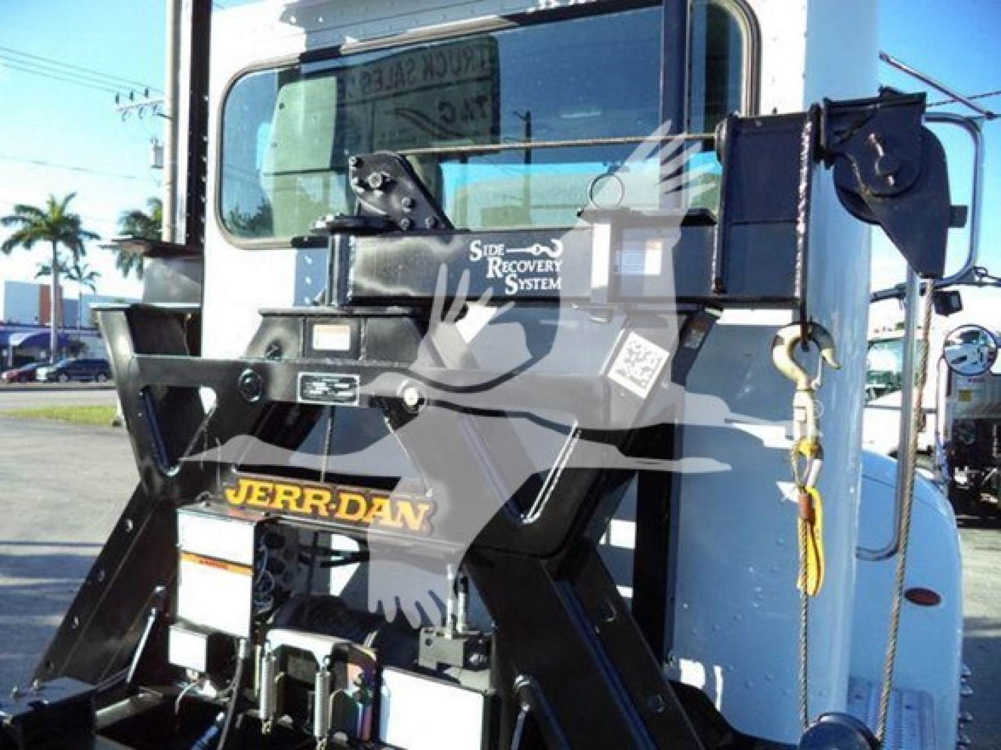 Back of a Rollback tow truck showing JERR-DAN tow unit with a Hai? label; windshield with reflection and various metal brackets and hydraulic components.