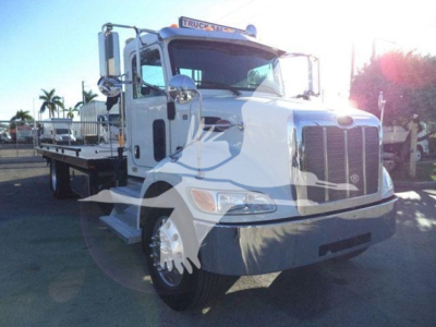 Truck front view of a white Peterbilt 337 rollback tow truck showing side deck and cab with chrome mirrors.