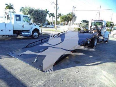 Peterbilt 337 rollback tow truck with a lowered flatbed in a dealership lot, white cab visible in background, VIN label area not legible.
