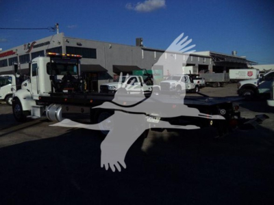 Peterbilt 337 rollback truck showing cab and flatbed in urban lot with other trucks