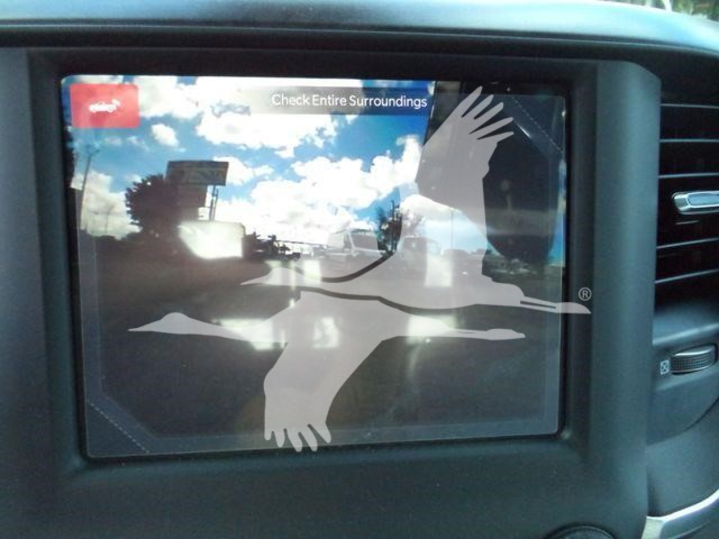 Truck interior: infotainment screen with a sticker of a crane and birds, showing a reflection of clouds and sky.