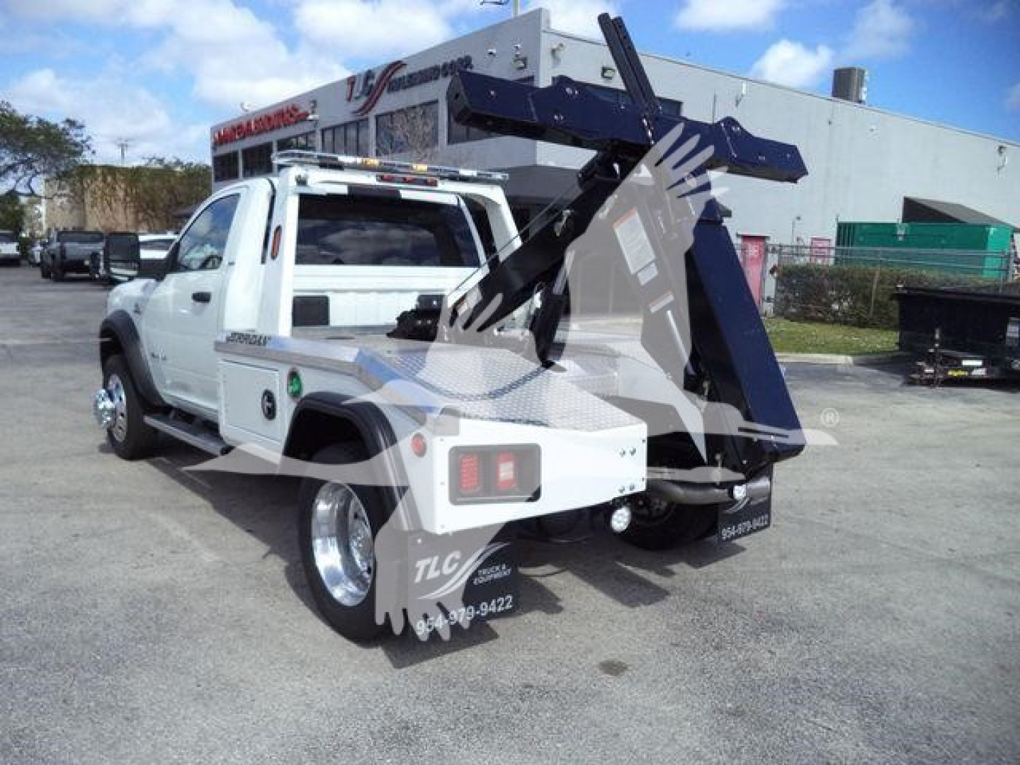 Truck bed with winch and auxiliary crane/tow setup mounted behind cab; white Ram 5500 SLT with heavy-duty rear equipment and hydraulic hoses.