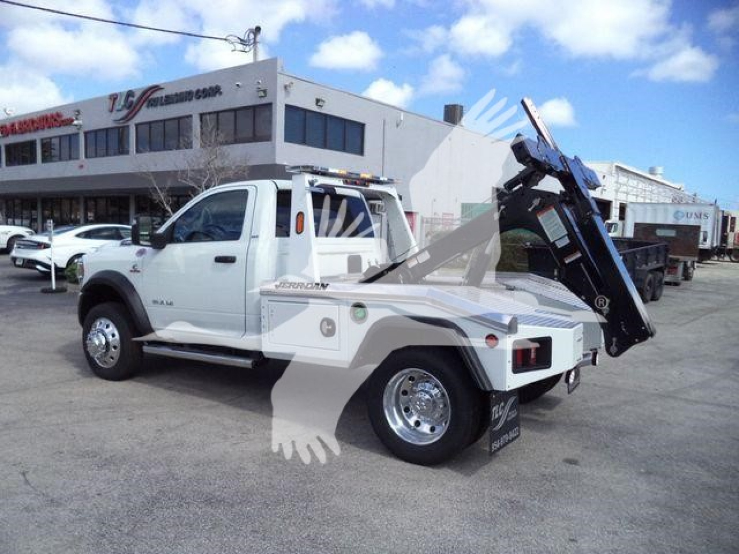 Ram 5500 tow truck with a raised crane/winch on the bed, white cab, flatbed with side steps, silver wheels, stock number J40087FM, dealership lot in background.