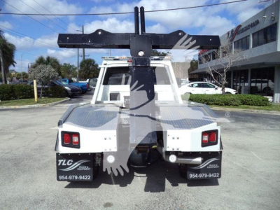 Ram 5500 tow truck rear view with heavy-duty tow hitch and winch gear, white body, black rack mounted on back, TLC branding on mud flaps, dealership lot in background.