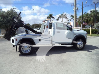 Ram 5500 tow truck with winch mount side view showing white cab and flatbed, dealership lot in background.