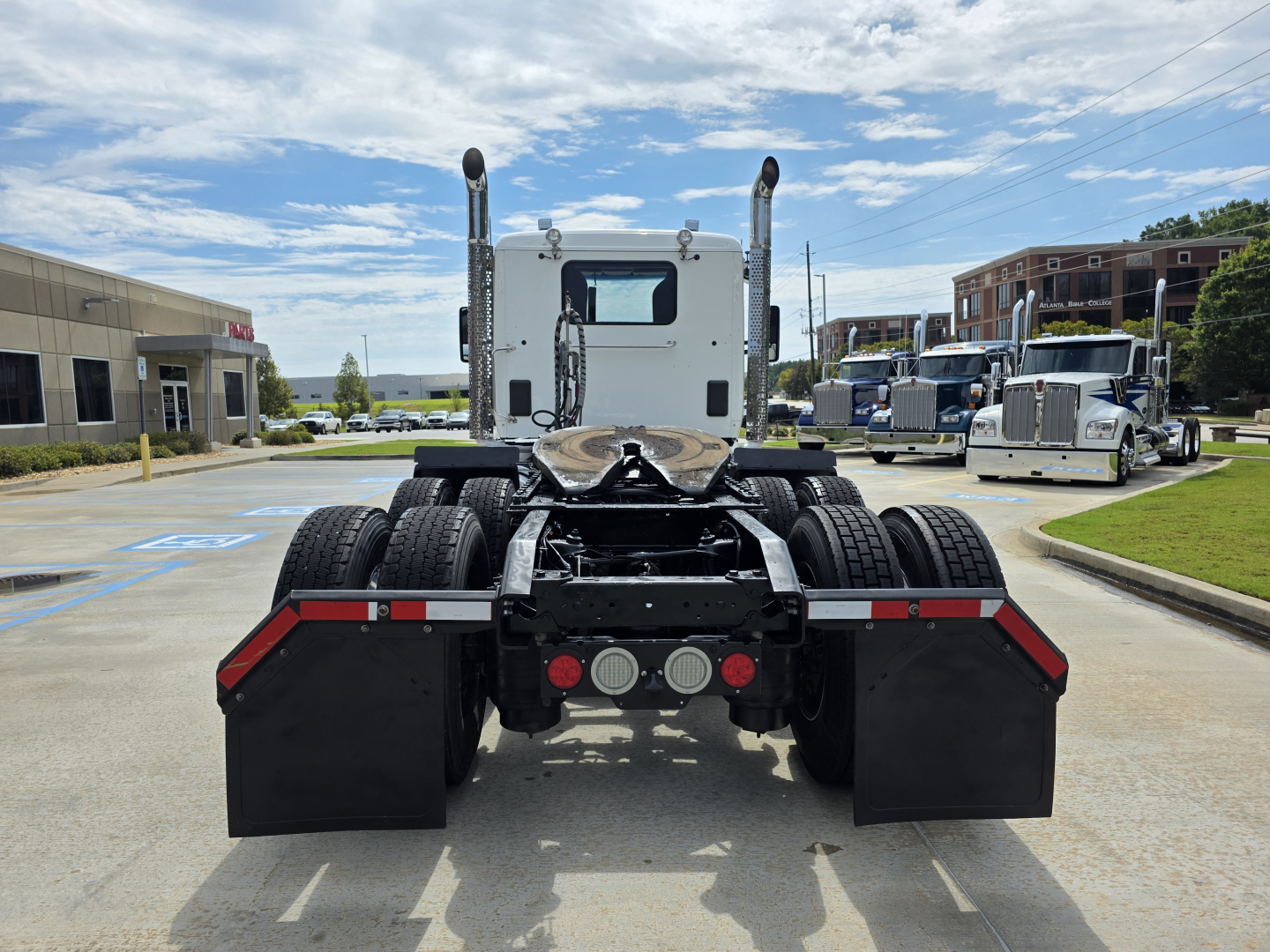 Kenworth T880 cab and chassis rear view showing dual rear axles and fifth wheel mounting with mud flaps and side-mounted exhaust stacks.