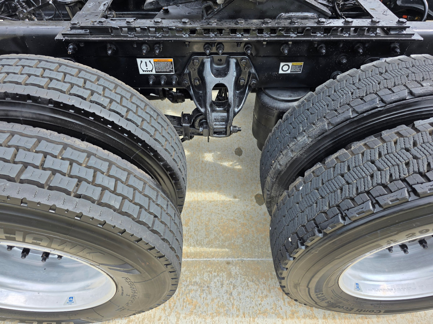View of a Kenworth tractor rear undercarriage focusing on dual rear axles and fifth-wheel area with tires and suspension components visible.