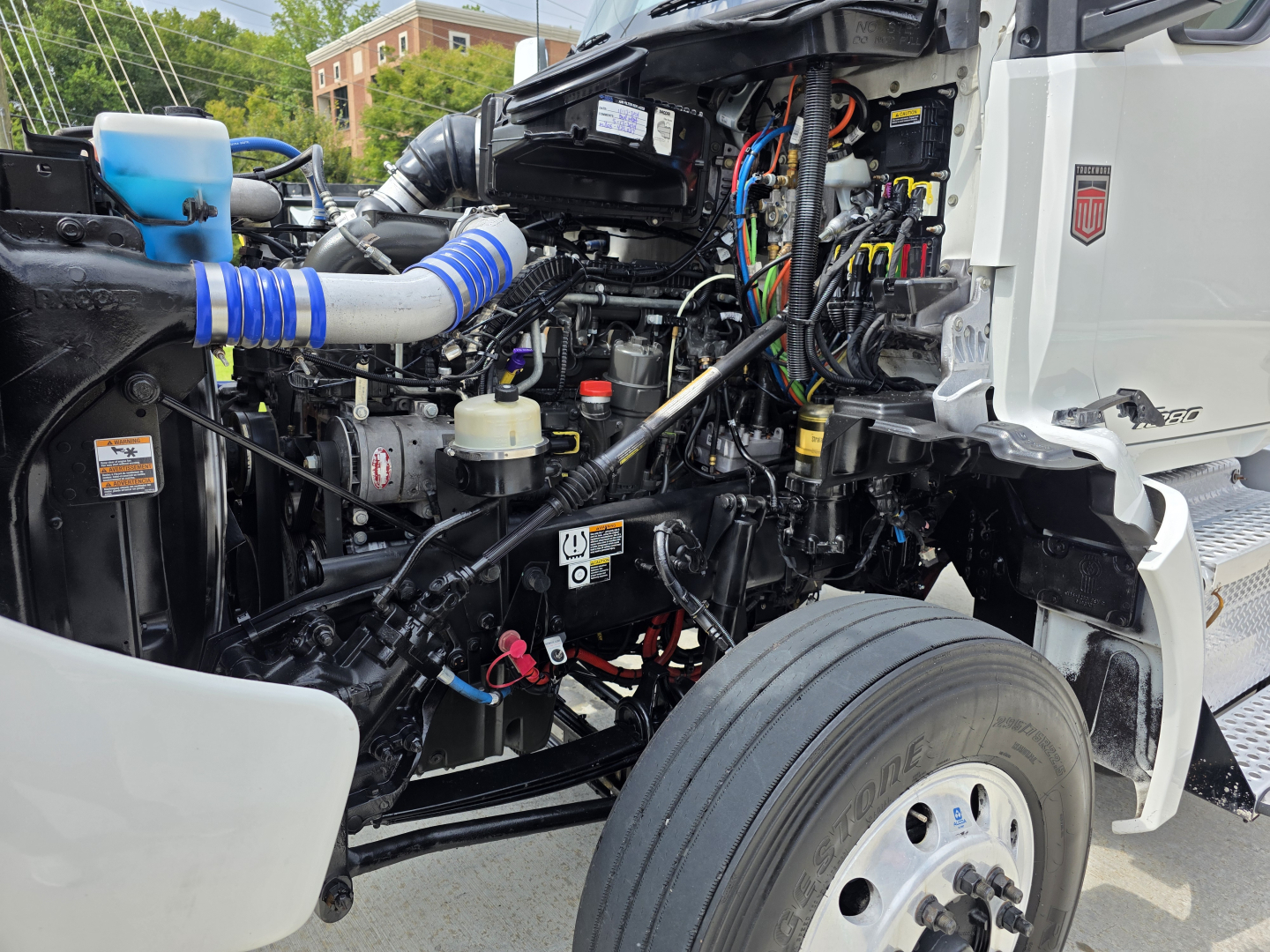Kenworth T880 engine bay view with exposed components, hoses, and wiring; visible cooling system hoses, reservoir, and chassis.