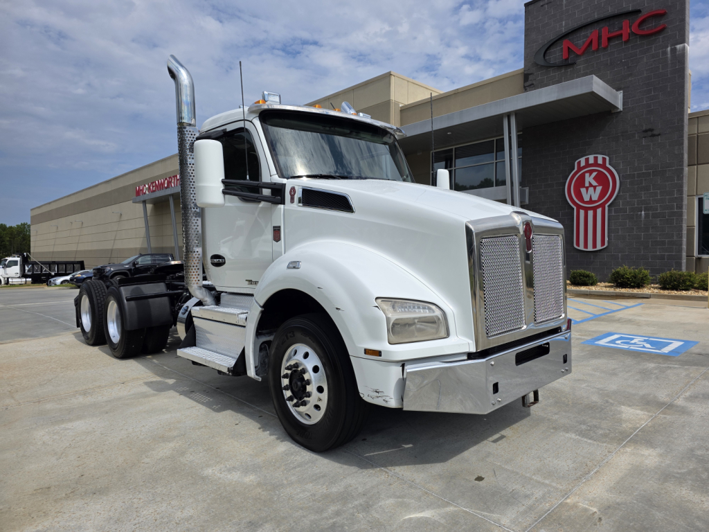 Kenworth T880 conventional daycab truck in a parking lot, white exterior, chrome grille, large exhaust stacks, front view.