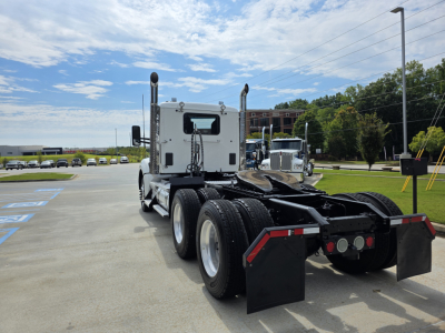 Kenworth T880 tractor rear view showing fifth wheel, dual rear axles, and mudflaps with truck yard in background.