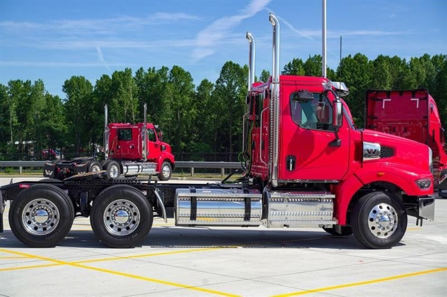 Truck cab and chassis of a new Western Star 49X day cab, bright red, shown in profile with twin vertical exhausts and chrome fuel tanks.