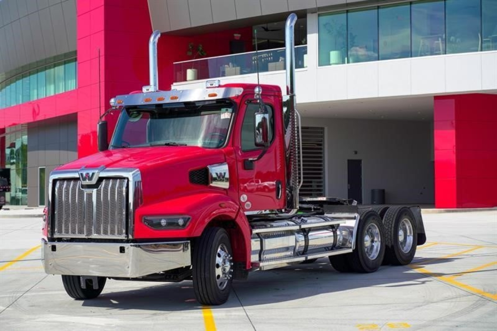 Red Western Star 49X day cab truck with chrome grille and dual exhaust stacks parked outside a modern building.