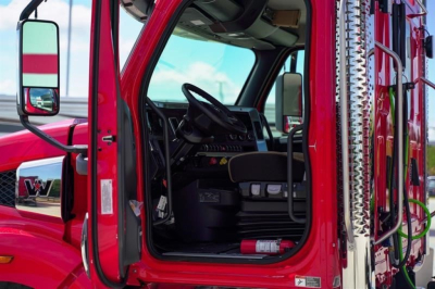 Cab view of a new 2027 Western Star 49X day cab truck showing the driver's seat and open door with red exterior