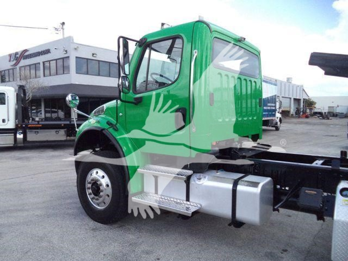 Green Freightliner M2 106 cab chassis with side steps and fuel tanks in view, front-left angle showing wheel and fender.