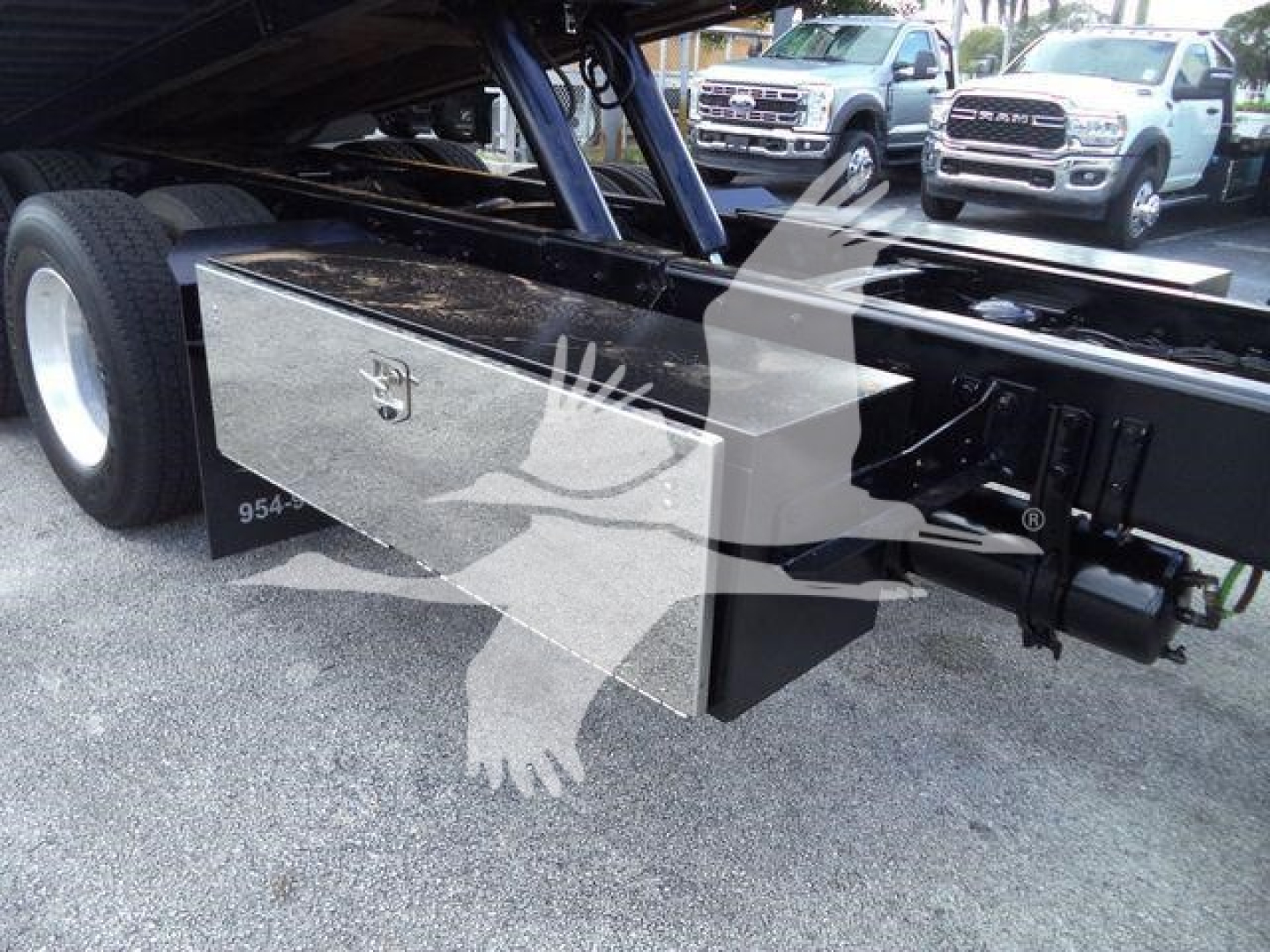 Flatbed area of a 2015 Freightliner M2 106 rollback truck showing a diamond-plate toolbox mounted underframe with hydraulic components and rear axles visible.