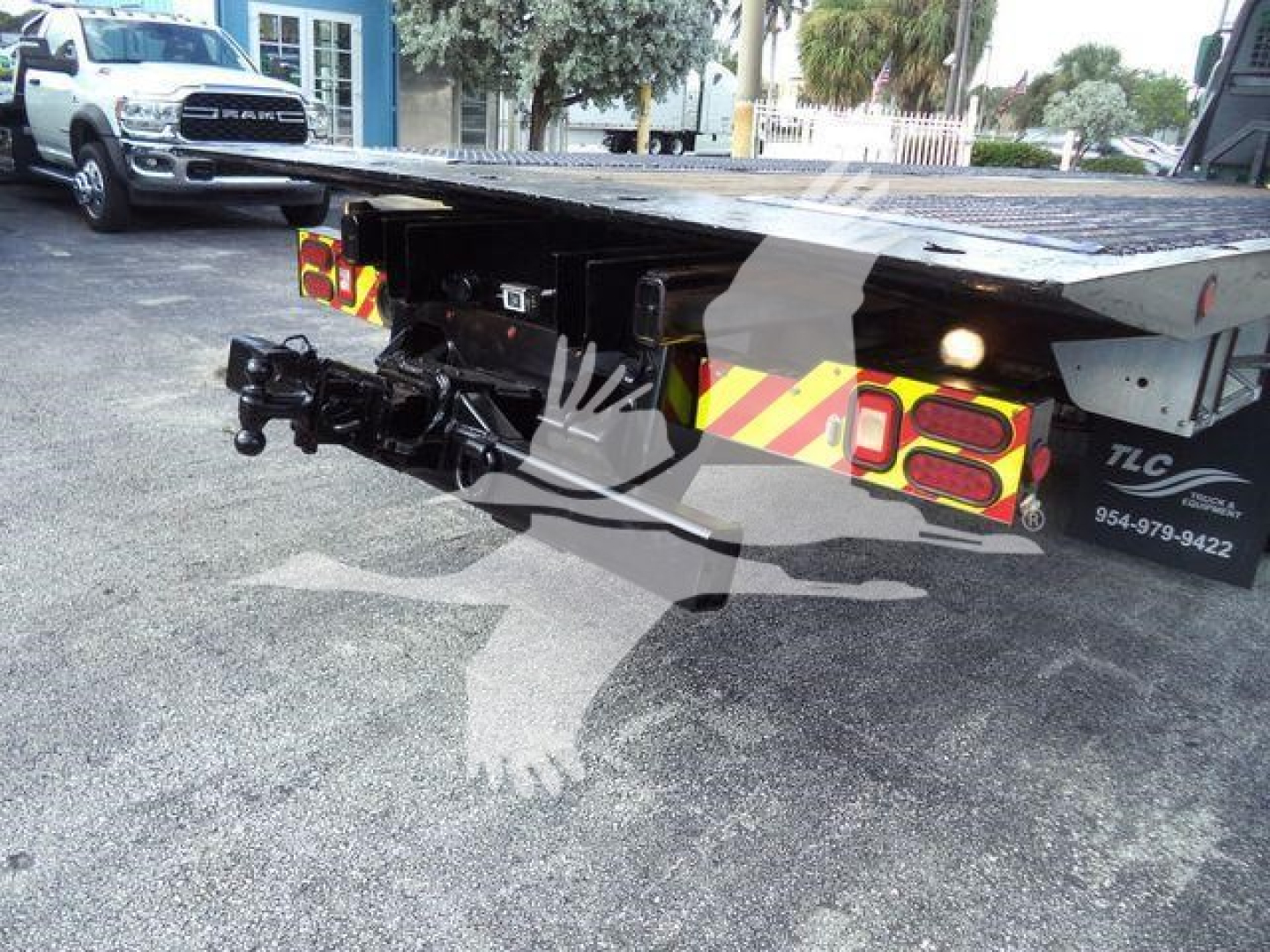 Flatbed tow truck trailer with hitch and rear lights, viewed from behind, showing platform and undercarriage components.