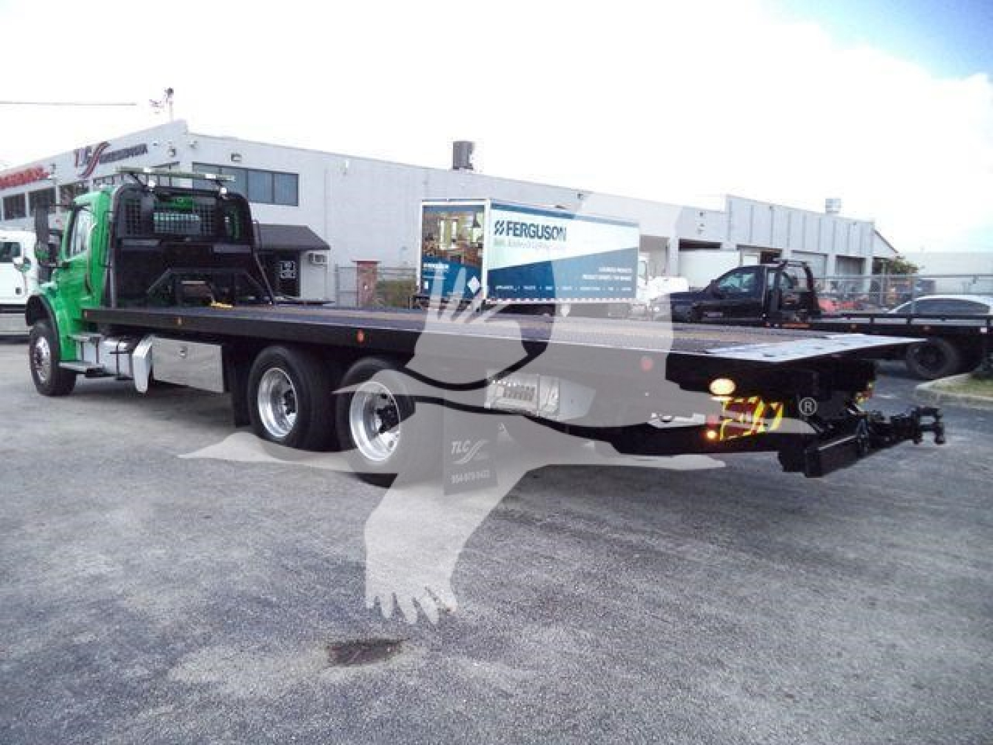 Flatbed tow truck in a dealership lot with Freightliner M2 106 chassis and roll-back bed. Visible text includes Ferguson trailer in background; stock number TD9494FM on listing signage.