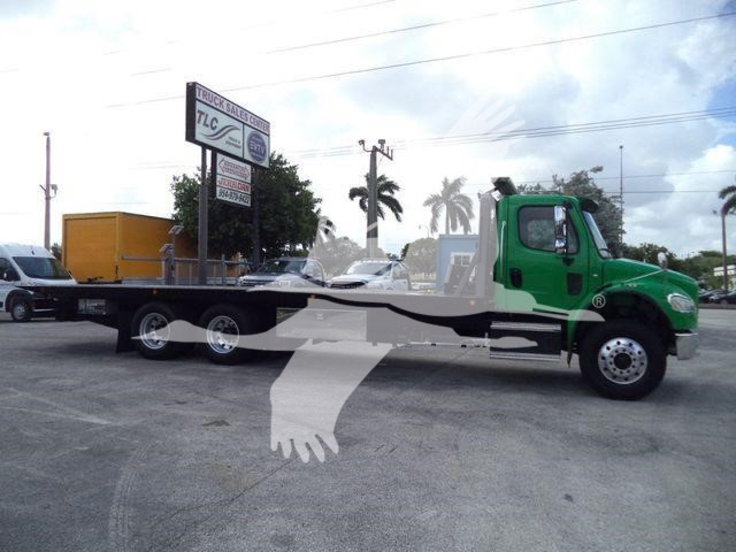 Side view of a green Freightliner M2 106 rollback truck with a long flatbed and wheel dollies, parked in a lot.