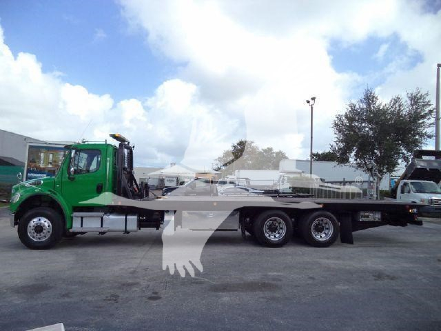 Freightliner M2 106 rollback truck, green cab, flatbed on a dealership lot.