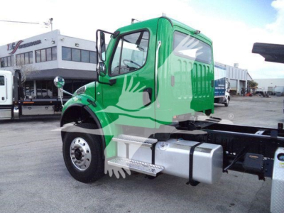 Green Freightliner M2 106 cab chassis with side steps and fuel tanks in view, front-left angle showing wheel and fender.