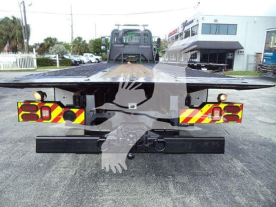 Flatbed tow truck chassis rear view showing warning chevron paint and rear bumper; tail lights and hitch visible on a Freightliner M2 106 rollback.