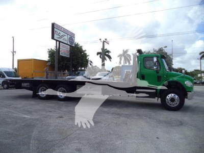 Side view of a green Freightliner M2 106 rollback truck with a long flatbed and wheel dollies, parked in a lot.