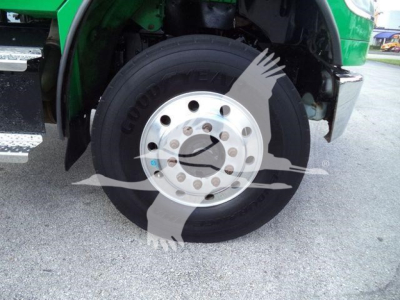 Wheel of a Freightliner M2 106 rollover truck showing tire and chrome hub, green fender, and front suspension area.