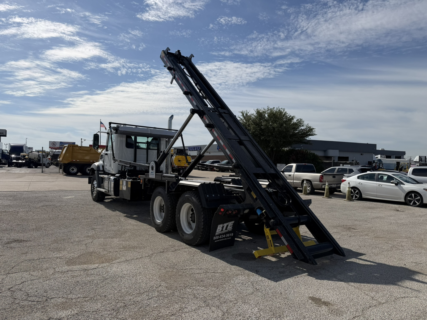 New 2026 Mack GR64B roll-off truck with a raised loading ramp in a parking lot, showing VIN 1M2GR2GC8TM054672 and stock number 70664.