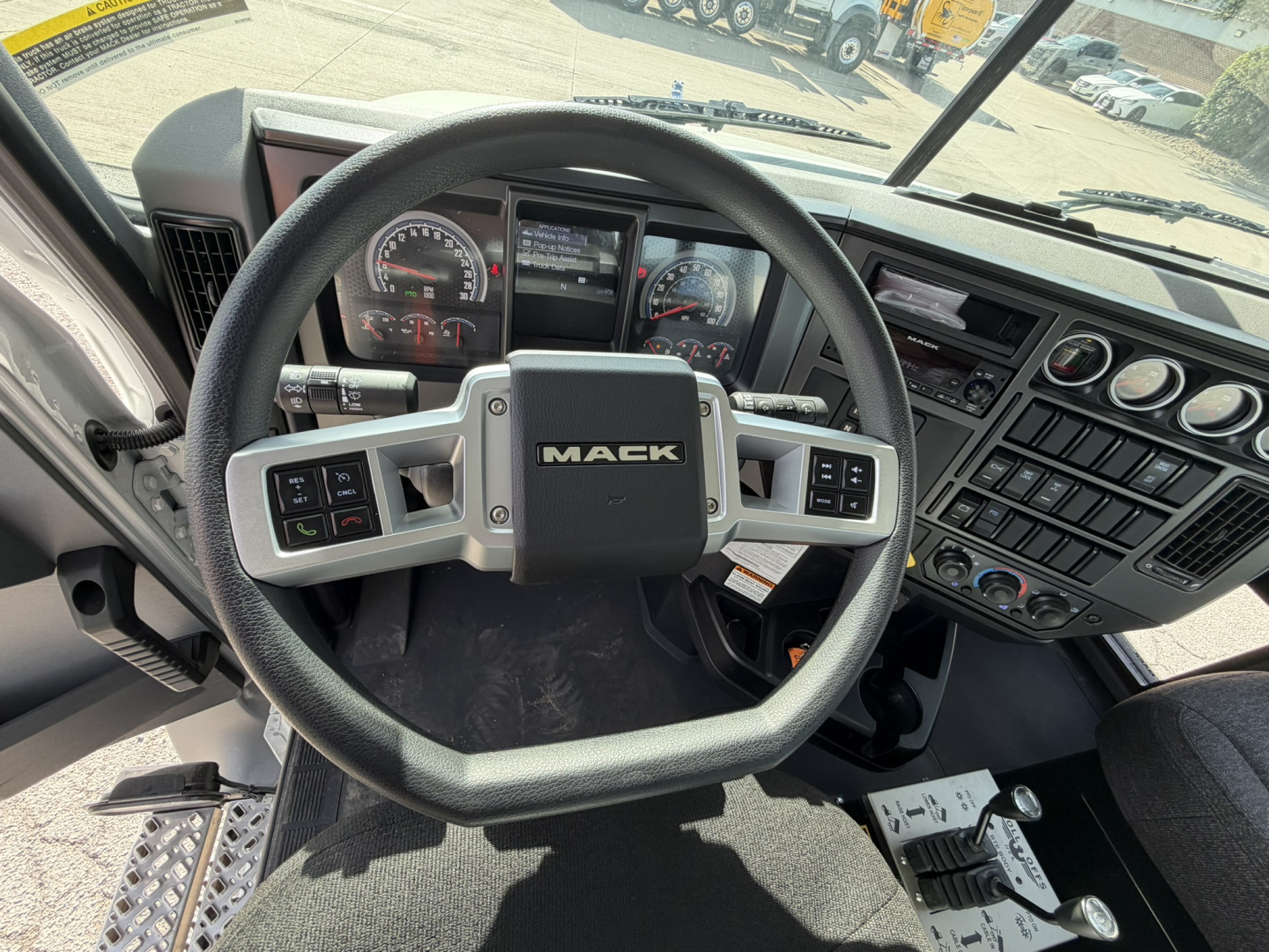 Mack GR64B truck interior showing steering wheel with Mack logo, dashboard gauges, and control panels.