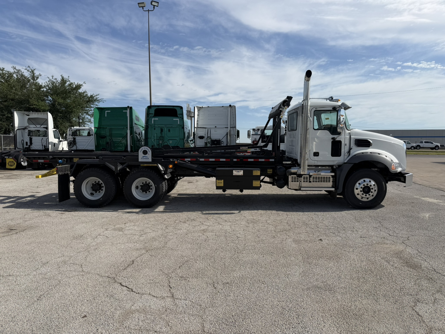 Mack GR64B roll-off truck side view showing cab, long wheelbase, and flatbed with hydraulic hooklift system.