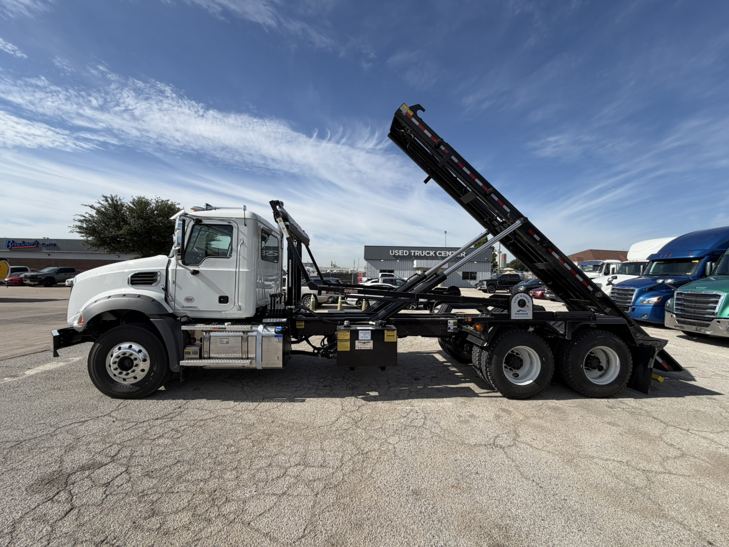 Mack GR64B roll-off truck side view showing hydraulic bed and chassis with black conveyor/hoist system.