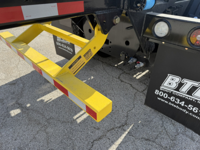 Yellow truck step/ladder onto a Mack GR64B roll-off truck with dealership sticker and safety labels visible.