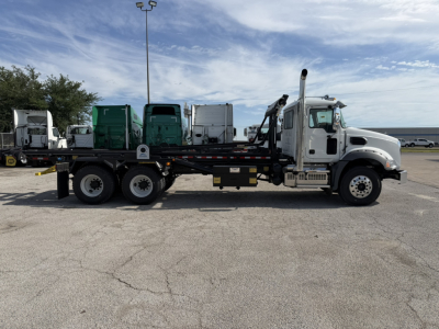 Mack GR64B roll-off truck side view showing cab, long wheelbase, and flatbed with hydraulic hooklift system.