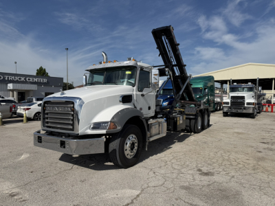 Mack GR64B roll-off truck in white, front-left view showing a raised hydraulic dump/boom, chrome bumper, and wheel arches.