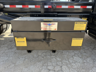 Rolloff truck toolbox mounted behind the cab with yellow caution labels. Box is black with handles, and warning stickers visible.