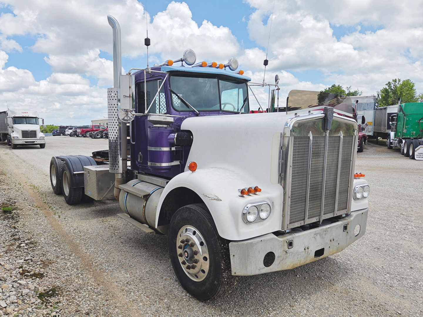 1960s Kenworth W-900A conventional daycab tractor in white and purple with chrome grille, dual exhaust stacks, and front bumper; photos shows cab with long hood, dual front wheels, and fuel tanks.