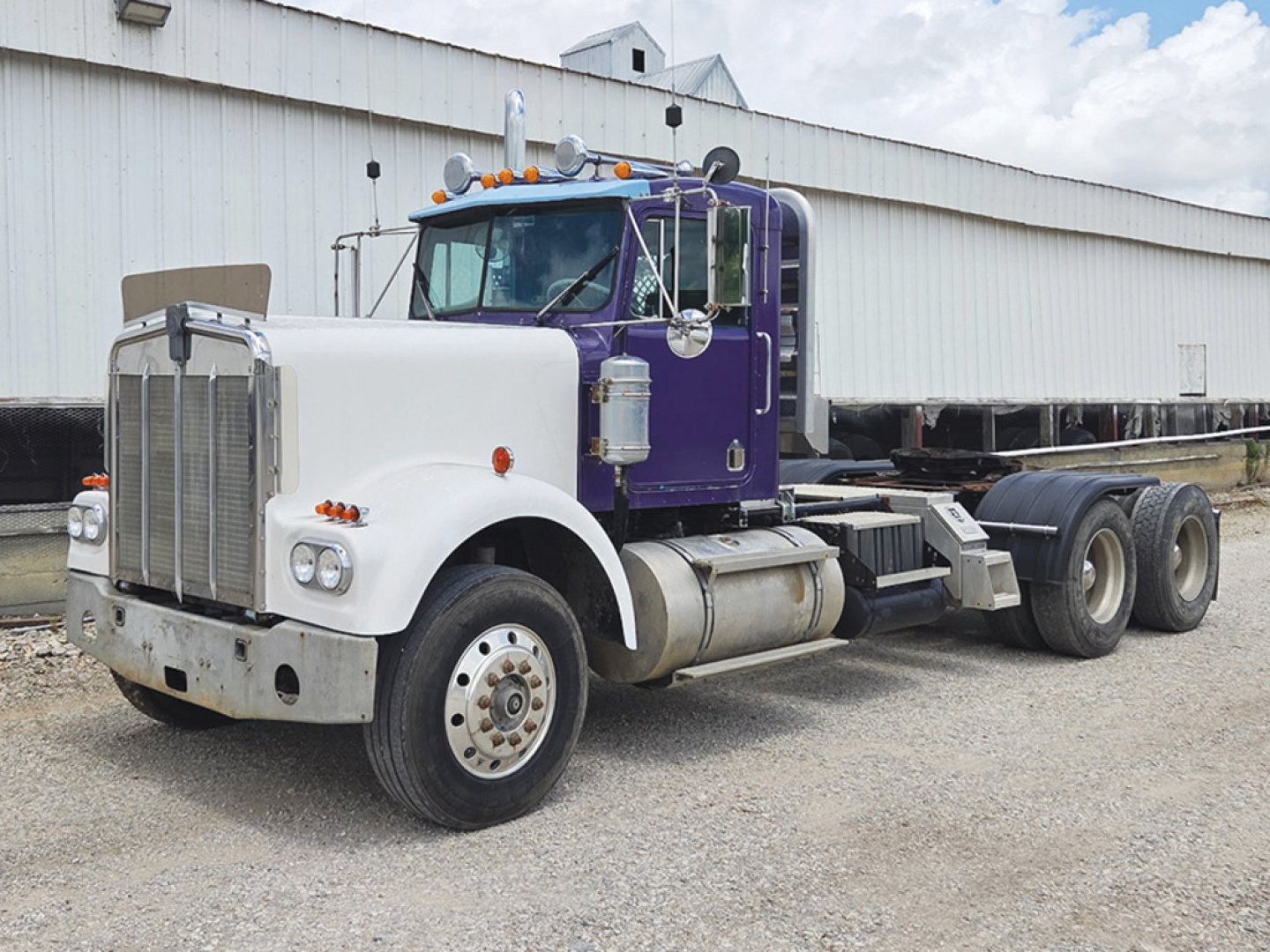 Truck cab and chassis of a 1978 Kenworth W-900A conventional daycab with purple and white color scheme; stock number 551059 visible on placard near front; VIN 161148S is not visible in image.