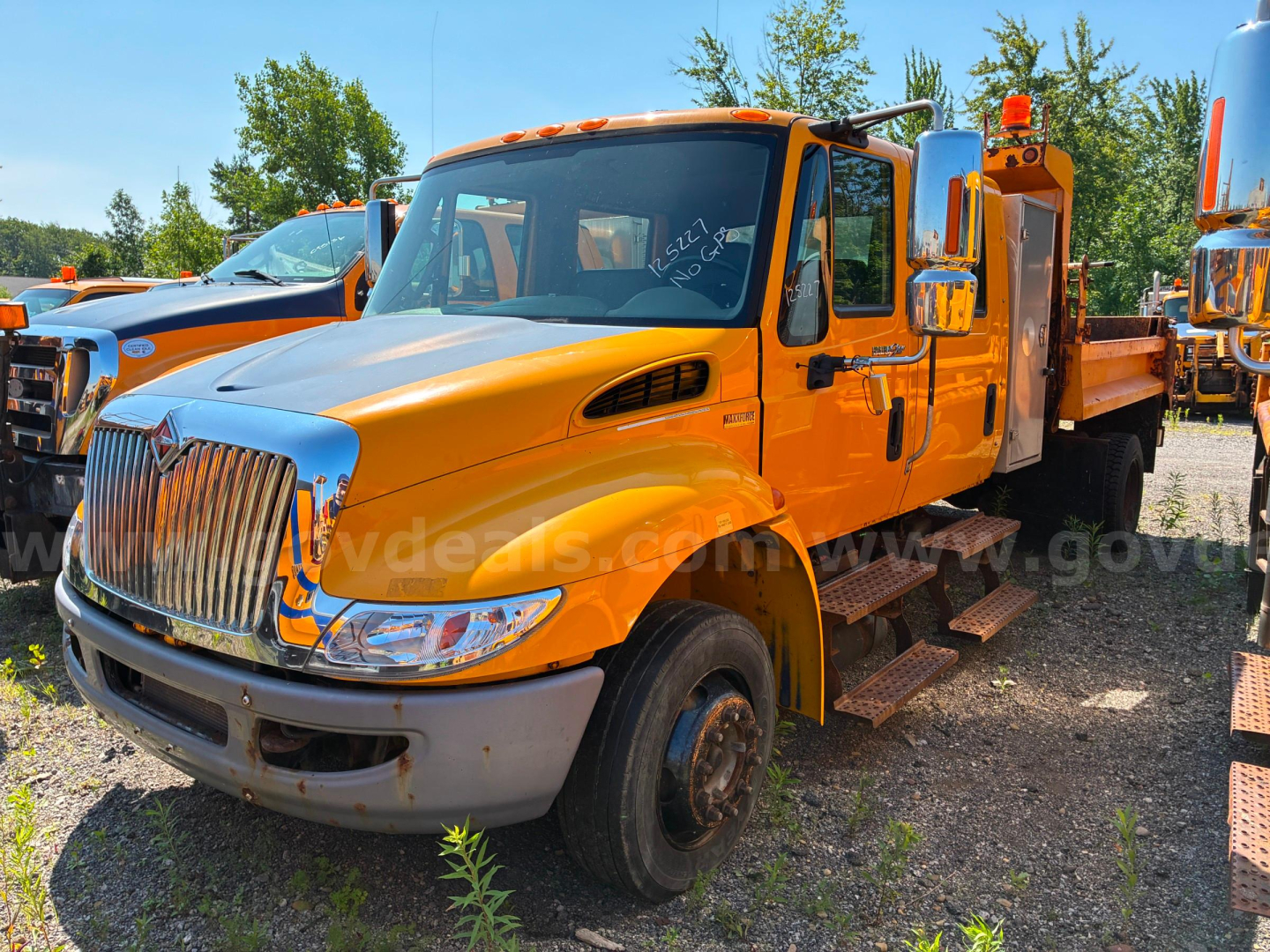 Orange 2012 International 4300 dump truck facing left with chrome grille, dual rear wheels, and side steps; VIN visible on windshield area.