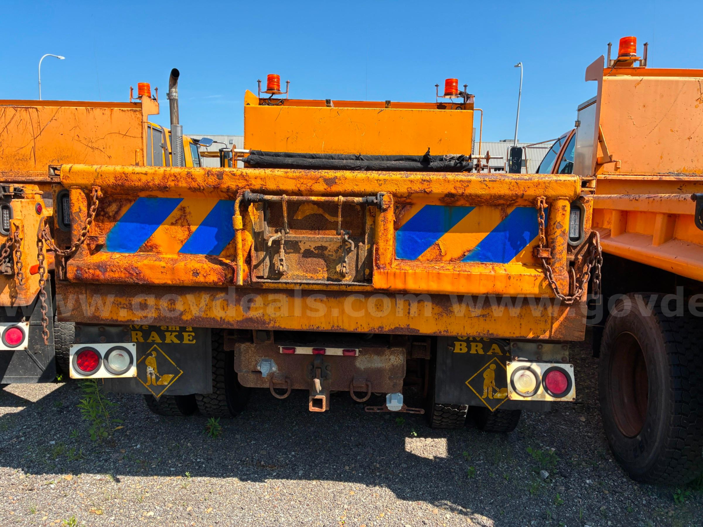 Rear view of a worn orange dump truck bed showing reflective blue stripes and taillight assemblies.
