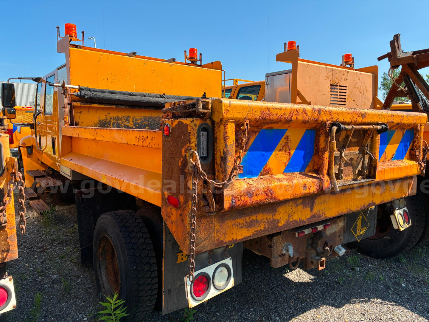 Dump truck bed of a 2012 International 4300 with orange body and reflective blue/yellow chevron stripes at rear, showing storage compartments and taillights.