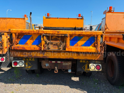 Rear view of a worn orange dump truck bed showing reflective blue stripes and taillight assemblies.