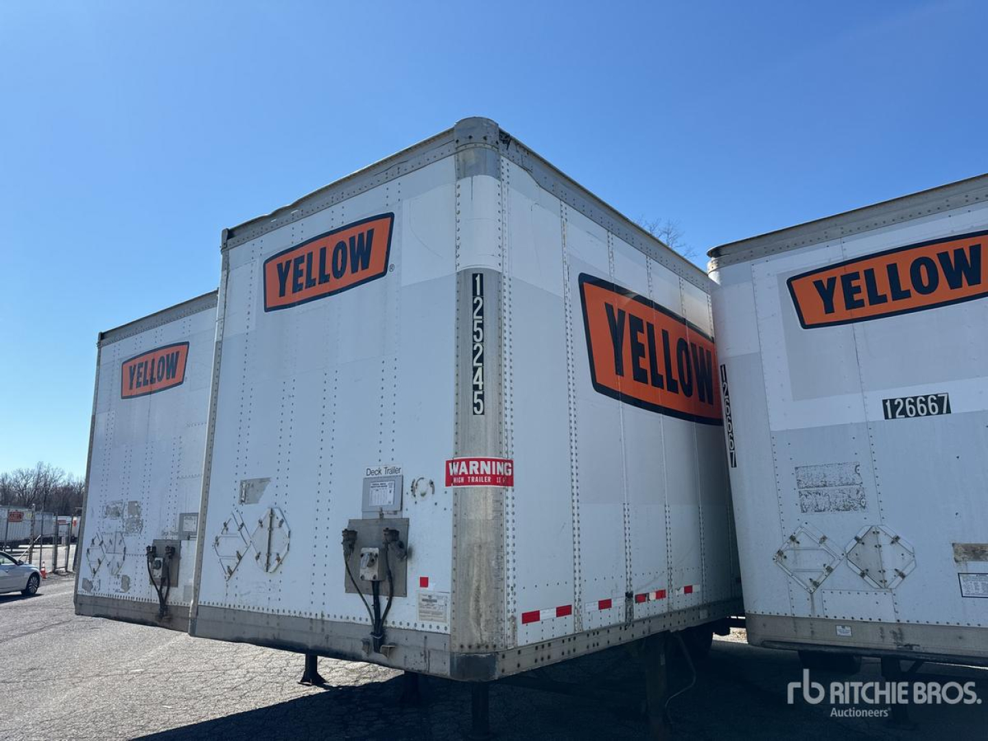 Rear view of a white Wabash van trailer with large orange YELLOW logos on the back and side doors, metal latches, and safety decals visible.